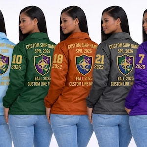 Peut inclure: Cinq vestes de coach en satin bleu clair, vert foncé, orange, gris anthracite et violet. Chaque veste présente au dos le texte CUSTOM SHIP NAME, SPR. 2026, FALL 2025, CUSTOM LINE NAME, un écusson en forme de bouclier avec une boussole et un grand chiffre.