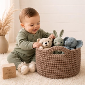 May include: A round, brown crocheted storage basket containing three stuffed animals: a beige bear, a sage green rabbit, and a blue elephant. Next to the basket is a small wooden block with the text little DREAMER engraved on the front surface.