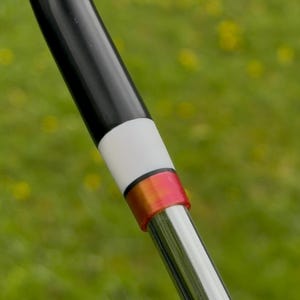 May include: A golf club shaft featuring a black upper section, a white band, a thin black ring, a metallic red-orange ferrule, and a polished chrome lower shaft section. The design transitions from a dark handle to a reflective metallic finish.