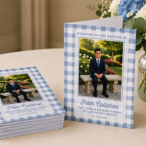 Puede incluir: Una pila de programas de bautizo plegados y uno vertical con un borde de cuadros vichy azul y blanco. La portada muestra una fotografía de un niño con traje sentado en un banco de piedra, con el texto Welcome to the Baptism of Peter Callahan, The Church of Jesus Christ of Latter-day Saints, y la fecha 01.12.2026.