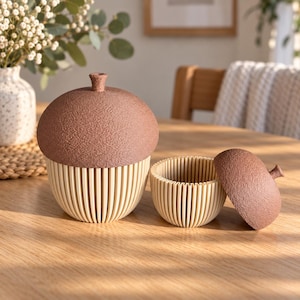 May include: Two acorn-shaped containers with textured brown caps and cream-colored, vertically ribbed bases. One container is closed, while the other is open with its brown cap placed beside the ribbed base, revealing the hollow interior.
