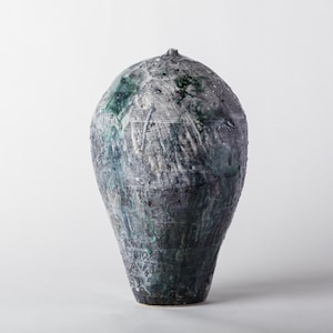 May include: A tall, bulbous ceramic vase with a narrow opening at the top. The surface features a textured, mottled finish in shades of dark charcoal gray, slate, and deep forest green, with visible vertical brushstrokes and white glaze accents.