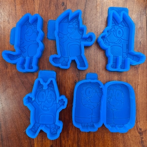 Könnte beinhalten: Ein Set aus fünf leuchtend blauen Kunststoff-Ausstechformen, die verschiedene Zeichentrick-Hundefiguren darstellen. Jede Form hat eine eigene Kontur und geprägte Innendetails der Figuren in verschiedenen Posen, wie Stehen, Springen und nebeneinander.