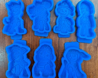 May include: A set of seven blue plastic cookie cutters, each shaped like a different character from the Paw Patrol series. The cutters feature detailed outlines of the various canine and human figures, including their uniforms, hats, and accessories.