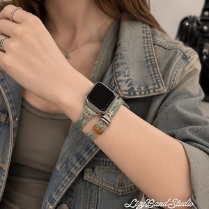 May include: A double-wrap watch band in a light green denim fabric featuring small silver-toned star embellishments and a brown leather accent loop. The band is attached to a rectangular smartwatch with a black screen. The text Lizy Band Studio is visible.