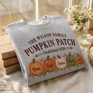 May include: A heather gray crewneck sweatshirt featuring embroidered text that reads THE WILSON FAMILY PUMPKIN PATCH Established 2026. Below the text are five pumpkins in orange, white, and green, each embroidered with the names Mom, Dad, Emma, Noah, and Lily.