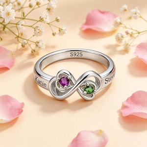 Peut inclure: Une bague infini en argent avec la gravure S925 sur l'anneau intérieur. La bague présente deux découpes en forme de cœur, l'une sertie d'une pierre violette et l'autre d'une pierre verte. Les prénoms Katie et Steve sont gravés sur l'anneau.