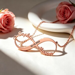 Puede incluir: Un collar de infinito en oro rosa con los nombres Sophia y Mason en letra cursiva integrados en los bucles, con la fecha 02.14.2025 grabada en la banda central, unido a una delicada cadena a juego en oro rosa.