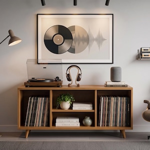 Puede incluir: Un mueble multimedia de madera con tres estantes abiertos que contienen discos de vinilo, una planta en maceta y libros. Encima hay un tocadiscos, auriculares en un soporte y un altavoz. Arriba cuelga un cuadro con un disco de vinilo.