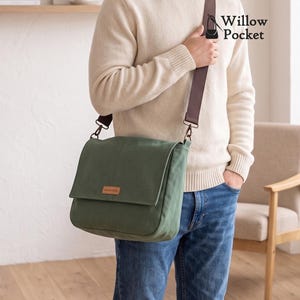 Op de afbeelding: Een saliegroene canvas schoudertas met een overslagklep, een bruine verstelbare schouderband en een klein rechthoekig bruin label aan de voorzijde. De tas is voorzien van de tekst Willow Pocket met een klein icoontje van een handtas rechtsboven.
