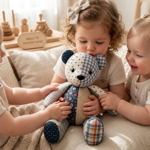 Puede incluir: Un oso de peluche de patchwork hecho con varios patrones de tela, incluyendo estrellas azules y blancas, cuadros vichy, estampados florales, lunares y rayas. El oso tiene una nariz negra y ojos oscuros, con un letrero de madera que dice MUJI YI MEMORY BEAR.
