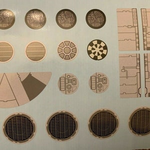 Könnte beinhalten: Eine Bogen mit Aufklebern mit verschiedenen Designs, darunter Kreise, Quadrate und eine Halbmondform. Die Aufkleber sind beige und braun mit filigranen Details.