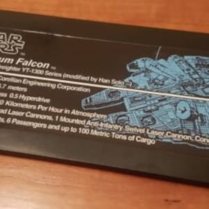 Könnte beinhalten: Eine schwarze Karte mit dem Text "STAR WARS" und "Millennium Falcon" in Weiß. Die Karte listet die Spezifikationen des Millennium Falcon auf, einschließlich Hersteller, Länge, Motor, Geschwindigkeit, Waffen und Kapazität. Die Karte zeigt auch eine Schwarzweißillustration des Millennium Falcon.