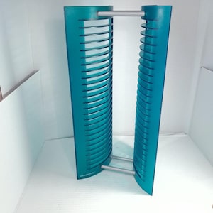 May include: A teal media storage rack featuring two vertical panels with horizontal slots for organizing discs. The panels are connected by two silver horizontal bars at the top and bottom. The word Atlantic is printed on the base of one panel.
