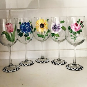 May include: Set of five wine glasses with hand-painted floral designs. Each glass features a different flower: a red tulip, blue hydrangea, yellow sunflower, purple flower, and pink rose. The glasses have black and white checkered bases.