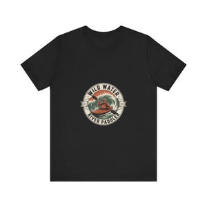 May include: A black short-sleeve t-shirt featuring a circular graphic on the chest. The design depicts a person in a kayak paddling through waves with the text WILD WATER RIVER PADDLER in a circular border and EST 1972 on the sides.