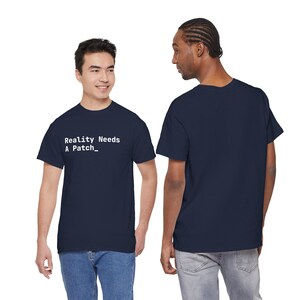 May include: A navy blue short-sleeved t-shirt featuring the white text "Reality Needs A Patch_" printed on the chest. The garment has a crew neckline and a standard fit, shown from both the front and back views to display the design and cut.