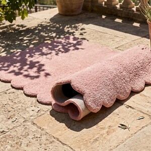 Modern nursery rug featuring a pink color palette, plush texture, and decorative scalloped edge. The cloud-inspired shape adds a whimsical element to nurseries, children's bedrooms, playrooms, and family spaces. It also works as a soft-looking accent in contemporary living rooms and reading corners. Pair it with pastel furniture, white storage units, light wood, stuffed animals, and neutral textiles for a sweet Scandinavian-inspired interior aesthetic.