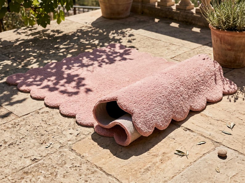 Modern nursery rug featuring a pink color palette, plush texture, and decorative scalloped edge. The cloud-inspired shape adds a whimsical element to nurseries, children's bedrooms, playrooms, and family spaces. It also works as a soft-looking accent in contemporary living rooms and reading corners. Pair it with pastel furniture, white storage units, light wood, stuffed animals, and neutral textiles for a sweet Scandinavian-inspired interior aesthetic.