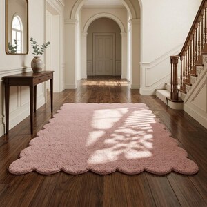 Modern scalloped edge rug in soft pink, featuring a plush appearance and flowing wavy border. This cozy floor accent is suitable for bedrooms, nurseries, living rooms, playrooms, and reading spaces. The gentle color pairs beautifully with neutral sofas, ivory textiles, wooden furniture, pastel artwork, and contemporary accessories. Its cloud-inspired silhouette creates a playful decorative element that complements Scandinavian, modern, minimalist, and soft contemporary interior styles.