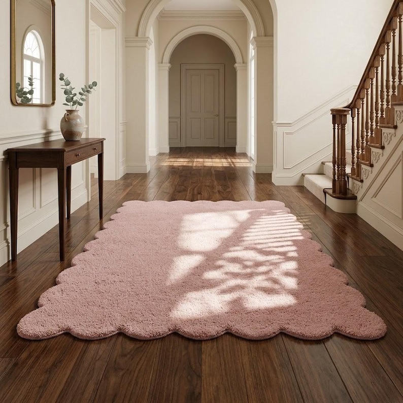 Modern scalloped edge rug in soft pink, featuring a plush appearance and flowing wavy border. This cozy floor accent is suitable for bedrooms, nurseries, living rooms, playrooms, and reading spaces. The gentle color pairs beautifully with neutral sofas, ivory textiles, wooden furniture, pastel artwork, and contemporary accessories. Its cloud-inspired silhouette creates a playful decorative element that complements Scandinavian, modern, minimalist, and soft contemporary interior styles.