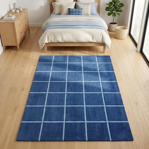 May include: A rectangular area rug featuring a deep blue base color with a grid pattern formed by thin, light blue lines. The rug is positioned on a light-toned wooden floor, displaying a consistent texture and a repeating square design across its surface.