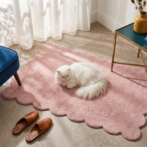 Plush pink area rug with rounded scalloped edges, offering a charming cloud-like appearance for contemporary home decor. This decorative floor mat works well in children's rooms, nurseries, bedrooms, living rooms, and dressing areas. Pair it with light wood furniture, cream cushions, white bedding, pastel decorations, and soft lighting for a coordinated look. Its organic outline adds visual interest to minimalist and Scandinavian interiors without overwhelming the surrounding decor.