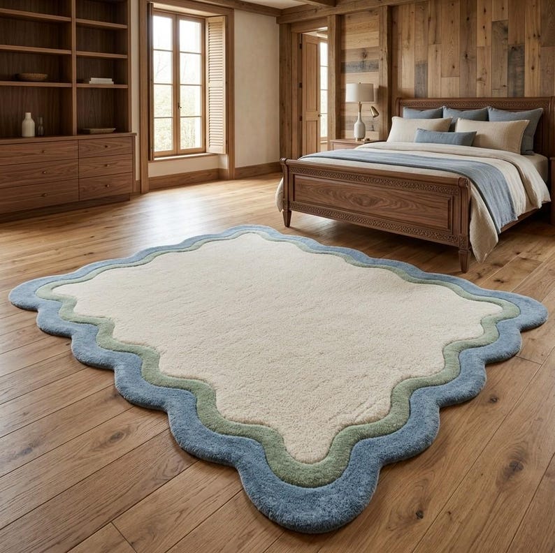 Scalloped area rug with wavy border in cream and sage green, placed in a bright room on wooden flooring