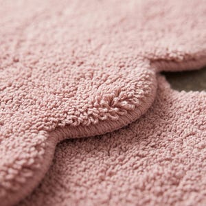 Scalloped pink floor rug featuring a cloud-inspired shape and plush decorative surface. This contemporary area carpet brings a soft visual accent to nurseries, bedrooms, living rooms, and cozy reading nooks. The wavy border adds playful character while the pink shade coordinates with white furniture, beige textiles, pale wood, and pastel accessories. Ideal for modern nursery decor, Scandinavian-inspired rooms, and interiors designed around a calm, welcoming color palette.