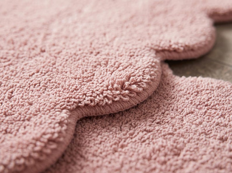 Scalloped pink floor rug featuring a cloud-inspired shape and plush decorative surface. This contemporary area carpet brings a soft visual accent to nurseries, bedrooms, living rooms, and cozy reading nooks. The wavy border adds playful character while the pink shade coordinates with white furniture, beige textiles, pale wood, and pastel accessories. Ideal for modern nursery decor, Scandinavian-inspired rooms, and interiors designed around a calm, welcoming color palette.
