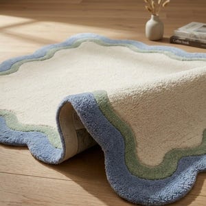 Close-up of scalloped rug shown rolled up, displaying the detailed blue wavy border and cream textured surface