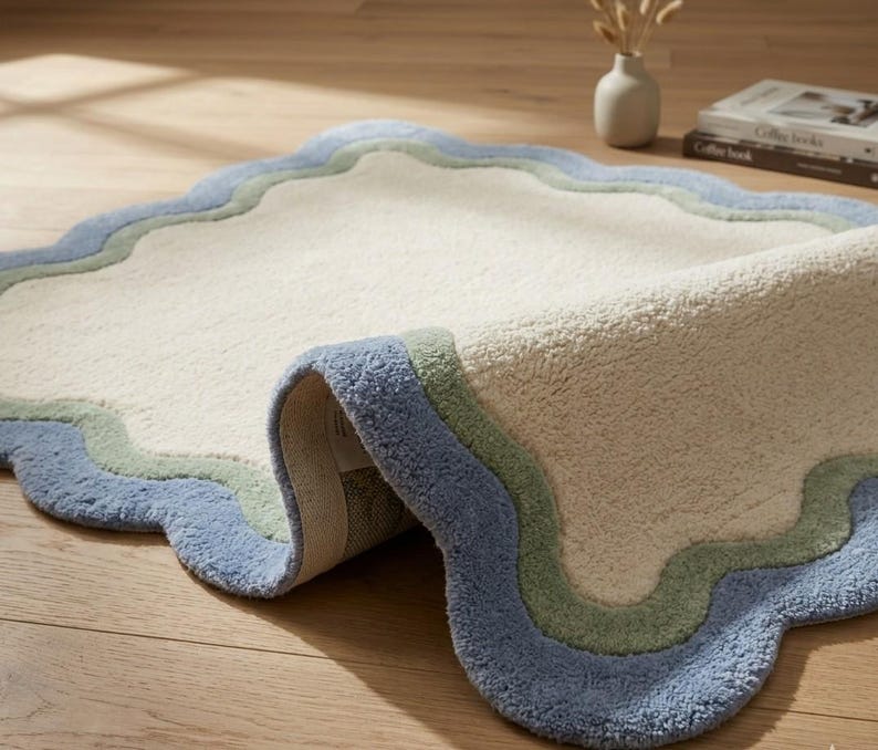 Close-up of scalloped rug shown rolled up, displaying the detailed blue wavy border and cream textured surface