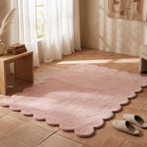 Pink plush cloud area carpet with a distinctive scalloped border, designed to create a cozy focal point in modern homes. The soft color and flowing edge detail complement nurseries, bedrooms, playrooms, living rooms, and relaxation areas. Style this decorative rug with cream upholstery, wooden furniture, pastel textiles, stuffed toys, and simple wall art. Its gentle design blends beautifully with Scandinavian decor and other interiors featuring soft neutral colors.