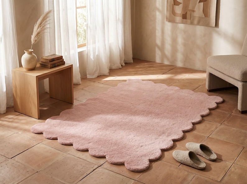 Pink plush cloud area carpet with a distinctive scalloped border, designed to create a cozy focal point in modern homes. The soft color and flowing edge detail complement nurseries, bedrooms, playrooms, living rooms, and relaxation areas. Style this decorative rug with cream upholstery, wooden furniture, pastel textiles, stuffed toys, and simple wall art. Its gentle design blends beautifully with Scandinavian decor and other interiors featuring soft neutral colors.