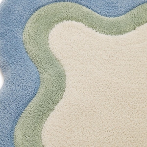 Top view of scalloped wavy edge rug showing sage green border pattern on cream textured base