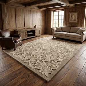 May include: A large rectangular area rug featuring a raised, tone-on-tone beige floral and scrolling vine pattern. The rug is positioned on a dark wood floor in a room with wood-paneled walls, a leather armchair, a wooden media console, and a sofa.