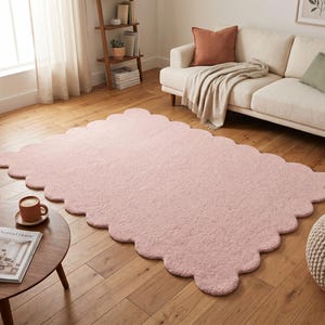 Modern nursery rug featuring a pink color palette, plush texture, and decorative scalloped edge. The cloud-inspired shape adds a whimsical element to nurseries, children's bedrooms, playrooms, and family spaces. It also works as a soft-looking accent in contemporary living rooms and reading corners. Pair it with pastel furniture, white storage units, light wood, stuffed animals, and neutral textiles for a sweet Scandinavian-inspired interior aesthetic.
