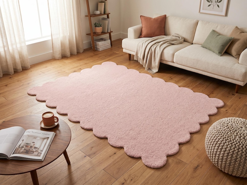Modern nursery rug featuring a pink color palette, plush texture, and decorative scalloped edge. The cloud-inspired shape adds a whimsical element to nurseries, children's bedrooms, playrooms, and family spaces. It also works as a soft-looking accent in contemporary living rooms and reading corners. Pair it with pastel furniture, white storage units, light wood, stuffed animals, and neutral textiles for a sweet Scandinavian-inspired interior aesthetic.