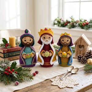 May include: Three crocheted figurines representing the Three Wise Men, each wearing a colorful robe and crown. The figures are crafted with detailed yarn textures, featuring embroidered facial features and small decorative accents held in their hands.