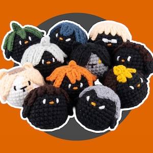 May include: A collection of eleven small, round, crocheted plush figures. Each figure features a black spherical body with a unique yarn hairstyle in colors including green, blue, cream, orange, brown, and gray, and small embroidered facial features.