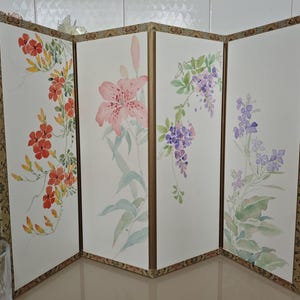 Peut inclure: Un paravent pliant à quatre panneaux présentant des illustrations à l'aquarelle de diverses fleurs. Chaque panneau affiche des motifs botaniques différents, dont des fleurs orange, un grand lys rose, de la glycine violette et de petites fleurs violettes.