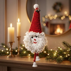 May include: A crocheted Santa Claus ornament featuring a tall red pointed hat with a white pom-pom, a thick white yarn beard, and a face with black eyes and a red mouth. Two small white bells hang from the bottom on red yarn strings.