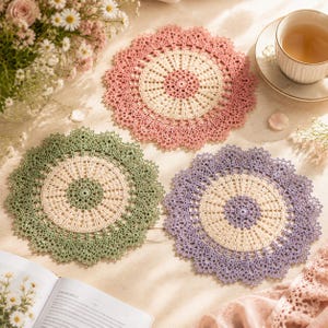May include: Three circular crochet doilies featuring intricate lace patterns. One doily is pink and cream, one is sage green and cream, and one is lavender and cream. Each piece has a central medallion design with a scalloped, lacy outer border.