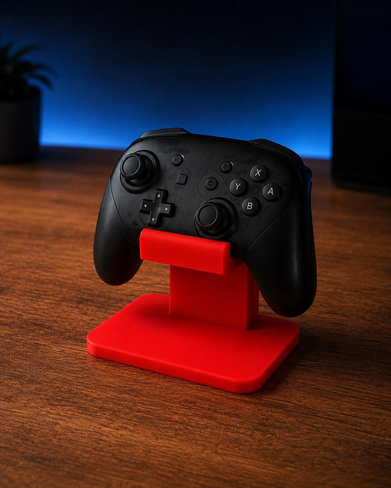 May include: A black wireless video game controller resting on a bright red plastic stand. The controller features two analog sticks, a directional pad, and four action buttons labeled A, B, X, and Y, along with central menu and capture buttons.