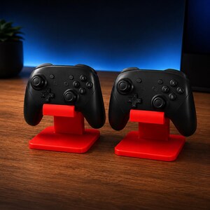 May include: Two black wireless game controllers, each resting on a bright red plastic stand. The controllers feature dual analog sticks, a directional pad, and four action buttons labeled A, B, X, and Y, along with several small system buttons.