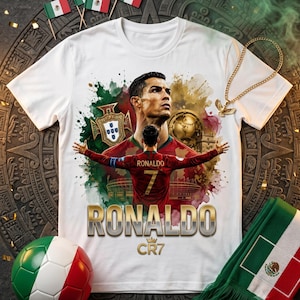 May include: A white t-shirt featuring a graphic print of Cristiano Ronaldo in a red Portugal jersey with his arms outstretched. The design includes the Portugal crest, a soccer ball, the text RONALDO, and the CR7 logo with a crown icon.