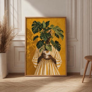 May include: A framed wall art print featuring a person wearing a yellow and white striped dress, holding a white patterned pot containing a large green monstera plant. The background is a solid mustard yellow color with a painted texture effect.