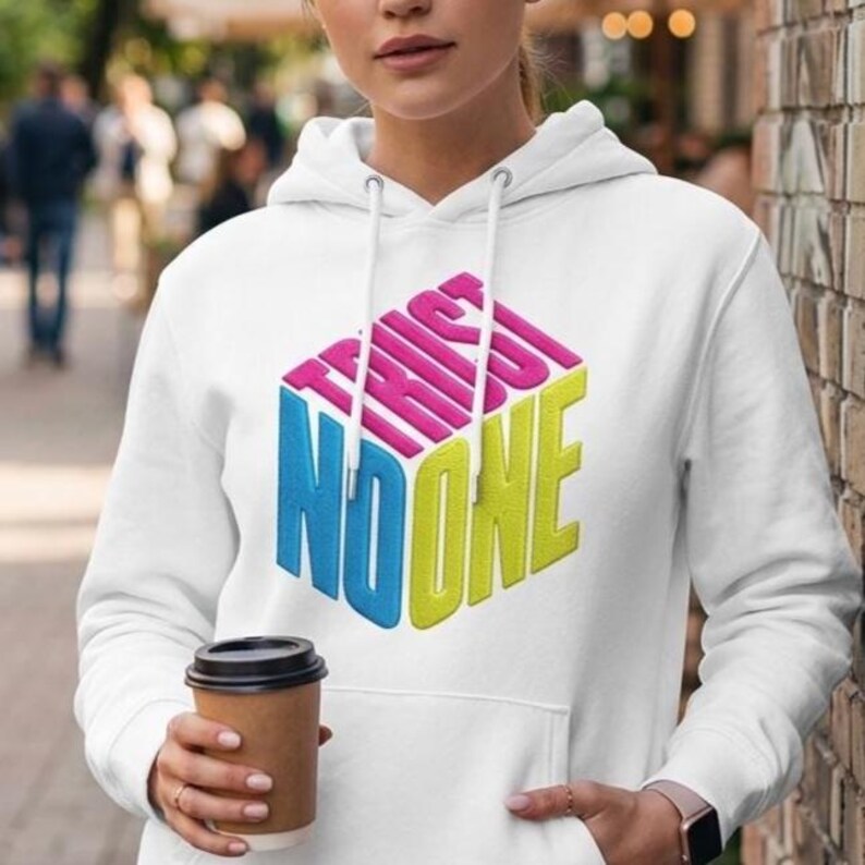 May include: A white hooded sweatshirt featuring a graphic of a three-dimensional cube with the text TRUST NO ONE printed on its faces. The text is rendered in pink, blue, and yellow, and the hoodie includes a front kangaroo pocket and drawstrings.