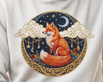 May include: A light gray hoodie featuring a circular embroidered design of a red fox sitting amidst clouds, stars, and a crescent moon. The artwork includes hanging decorative ornaments and a gold-toned filigree border on a dark blue background.
