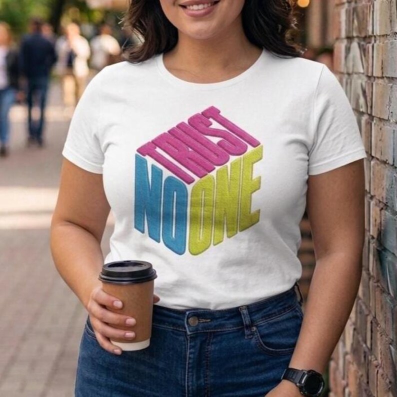 May include: A white short-sleeve t-shirt featuring a graphic design of a three-dimensional cube. The text "TRUST NO ONE" is printed on the cube faces in pink, blue, and yellow, creating a geometric visual effect on the front of the garment.